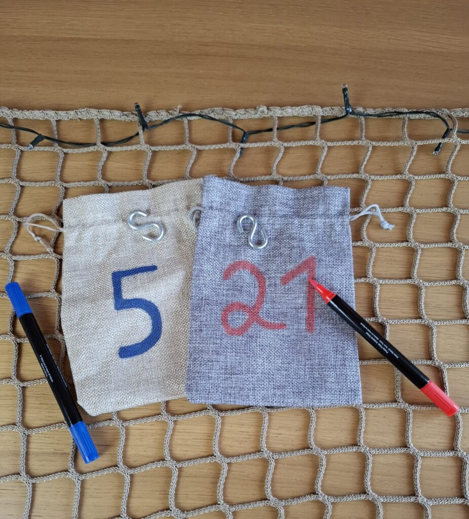 Material für den DIY-Adventskalender: Netz, Jutesäckchen, S-Haken, Acrylstifte und Lichterkette