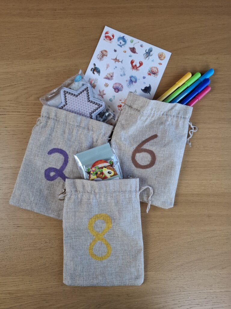 Geöffnete Adventskalender-Säckchen mit Bügelperlen, Stiften und Stickern